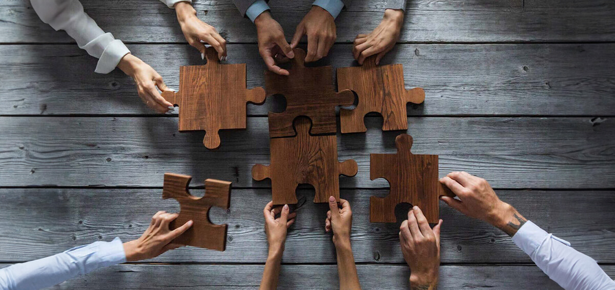 Various hands solving a large wooden jigsaw