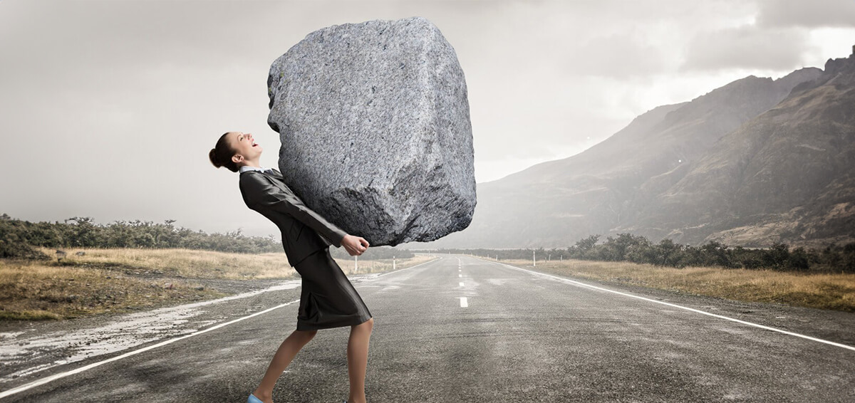 Woman carrying a very large rock across a road