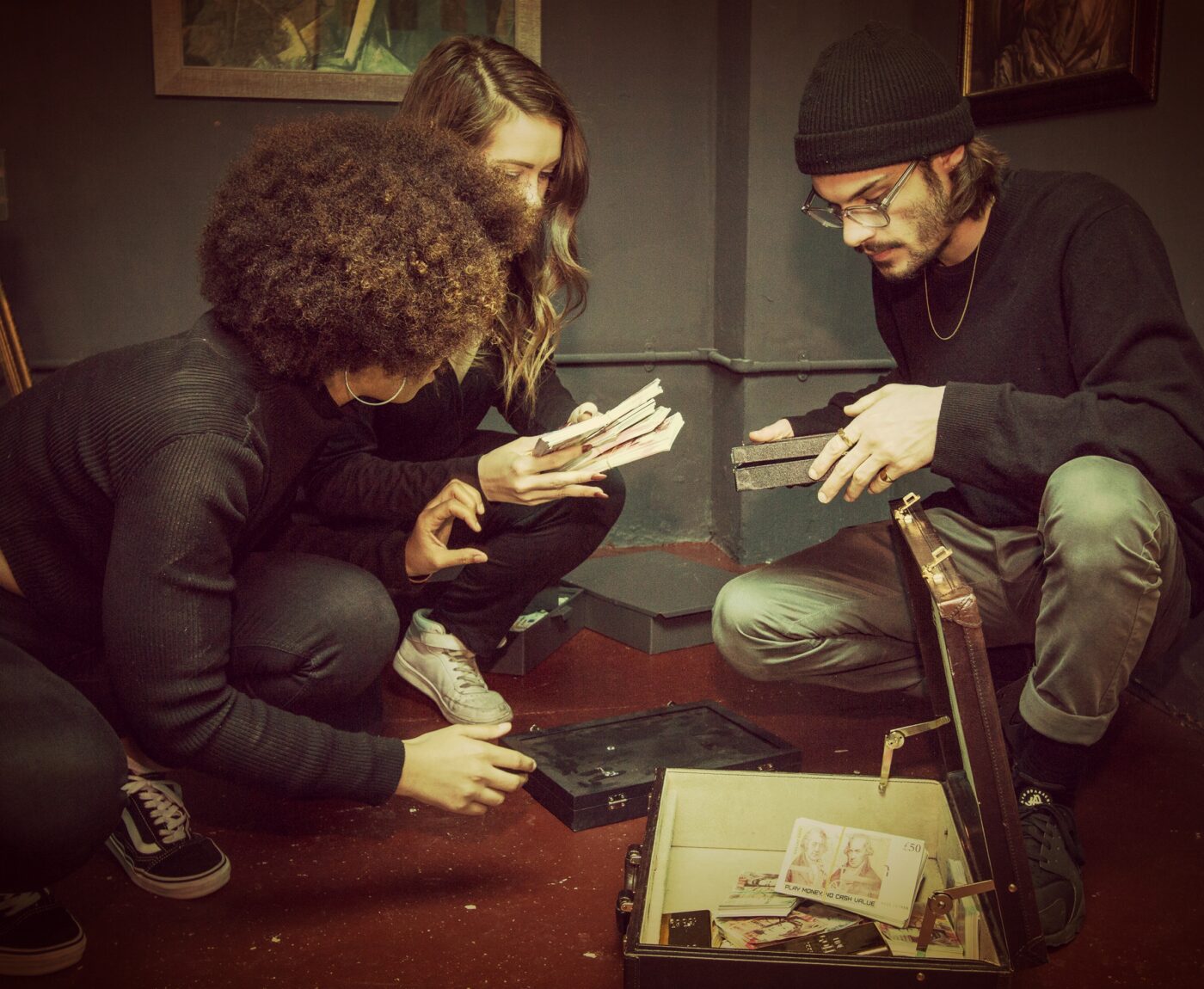 Three people crouched around an open suitcase full of money